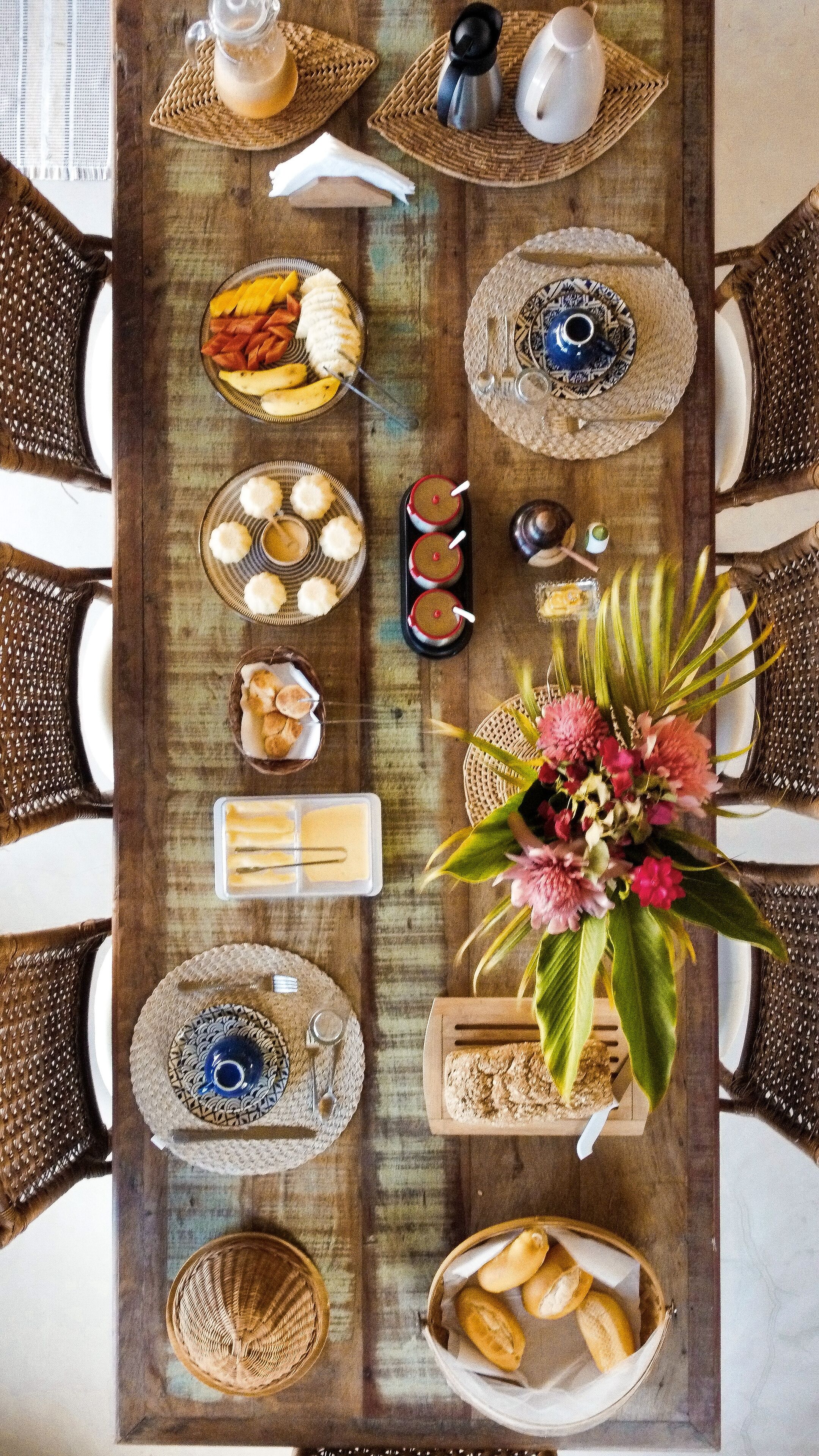A wooden dining table set with various dishes, utensils, and a floral centerpiece.