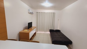 A small, clean room with a bed, a desk with a computer and phone, and a window with curtains. - Náutico Flat Caldas Novas - HotFérias (Caldas Novas)