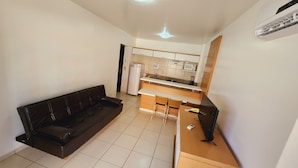 A compact living space with a sofa, a small dining table with two chairs, a kitchenette with a microwave, and a refrigerator. - Náutico Flat Caldas Novas - HotFérias (Caldas Novas)