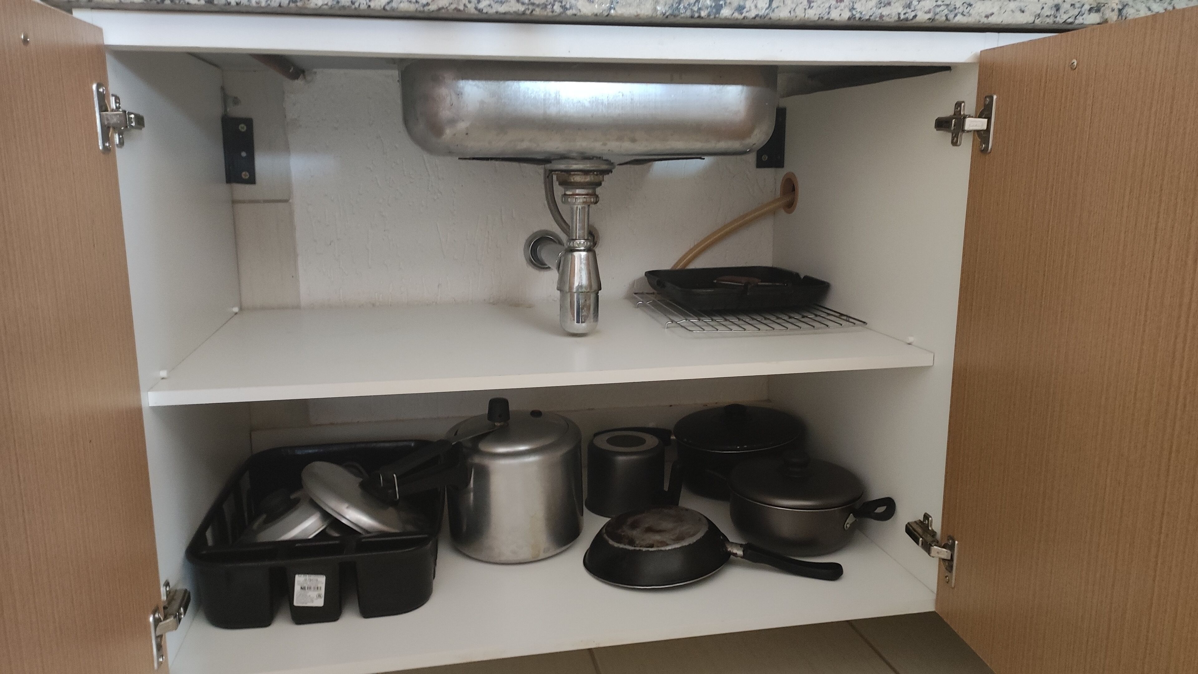 A kitchen with a stainless steel sink, a frying pan, and various pots and pans on shelves.