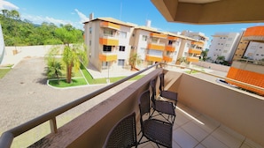 A balcony with wicker chairs, a tiled floor, and a view of multi-story buildings with orange and white facades. - Náutico Flat Caldas Novas - HotFérias (Caldas Novas)