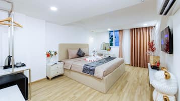 A modern hotel room with a bed, bedside table, dresser, and a desk with a chair.