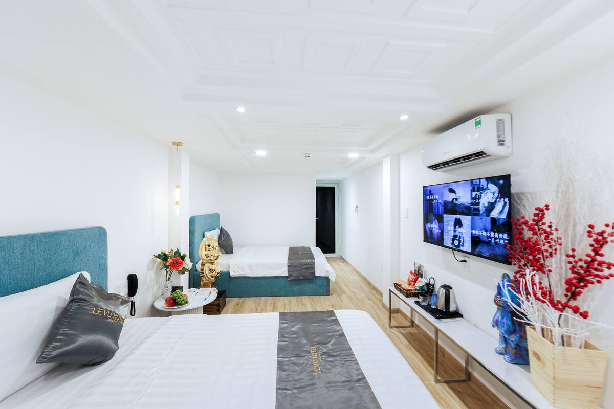 Ein Hotelzimmer mit einem großen Bett, einem kleineren Bett, einem an der Wand montierten Fernseher und einem Nachttisch aus Holz mit einer Vase und einem Telefon.