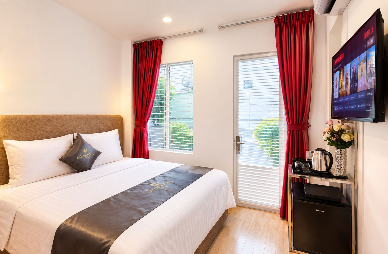 A hotel room with a bed, a TV, a minibar, and a window with curtains.
