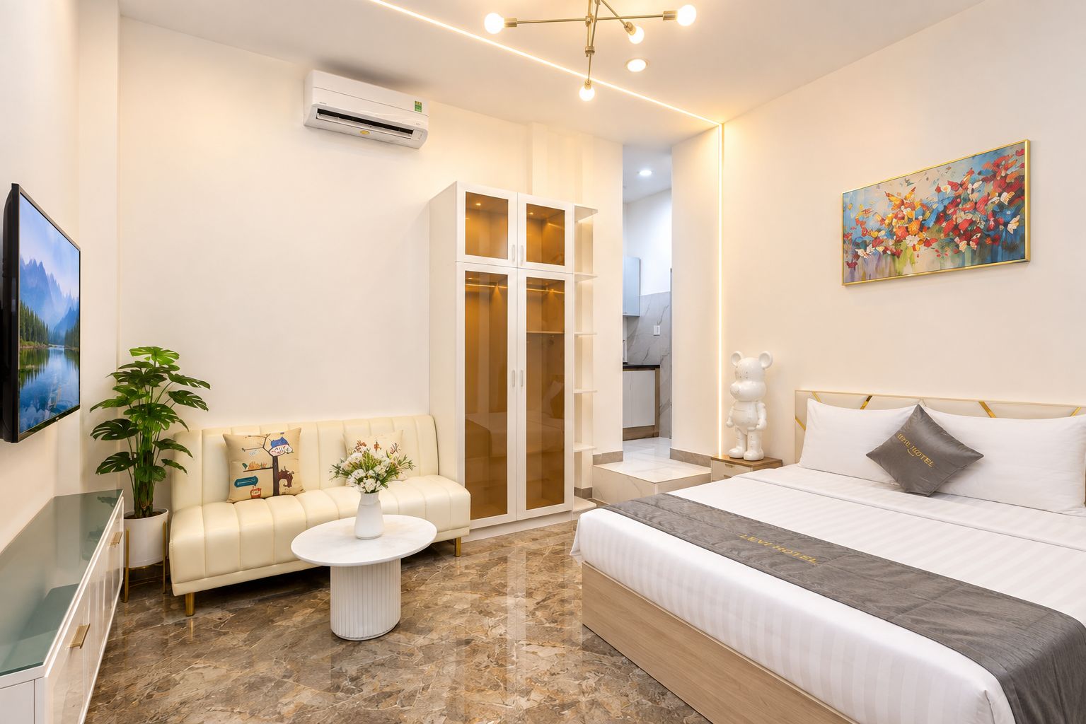 A hotel room with a bed, a sofa, a small table, a potted plant, and a painting on the wall.