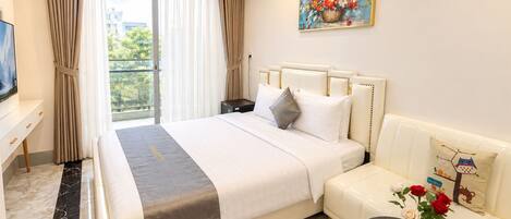 Habitación de hotel con una cama grande, un sofá, una mesita, un cuadro y vistas al exterior con vegetación.