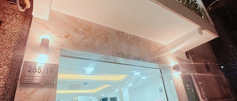 Una entrada de hotel con fachada de mármol, un mostrador de recepción y una escalera que conduce a los pisos superiores.
