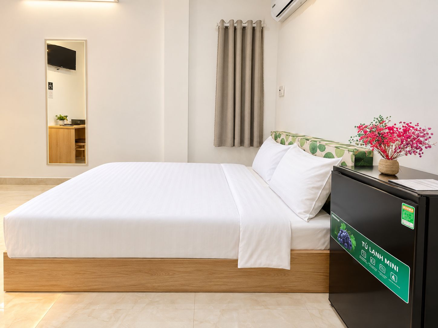 Una habitación de hotel con una cama, un escritorio con computadora, un espejo, una ventana con cortinas y un equipo de aire acondicionado.