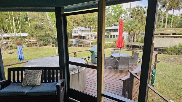 Une terrasse extérieure couverte, dotée d’un espace salon, d’une table et offrant une vue sur une maison et la verdure environnante.