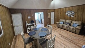 Une pièce chaleureuse avec un plancher en bois, une table ronde entourée de chaises, un canapé et un mur décoré de motifs de poissons.