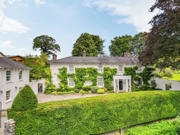A white building with a symmetrical facade, multiple windows, and a well-maintained hedge in the foreground.