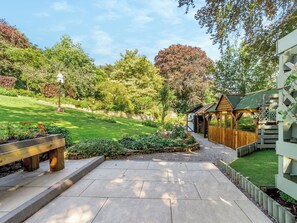 Ein Garten mit einem hölzernen Gartenhaus, einem gepflasterten Weg und einer Rasenfläche.