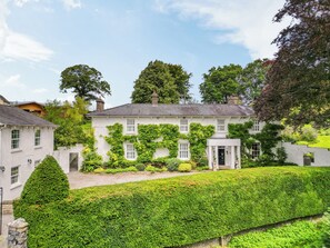 A white building with a symmetrical facade, multiple windows, and a well-maintained hedge in the foreground.