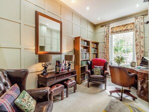 A well-furnished living room with a leather sofa, a wooden desk, a bookshelf, and a large mirror.
