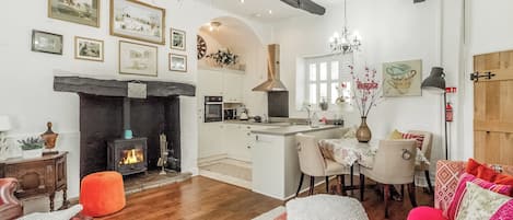 Ein gemütliches Wohnzimmer mit Kamin, Holzbalken, einer Essecke und einem farbenfrohen Sofa.