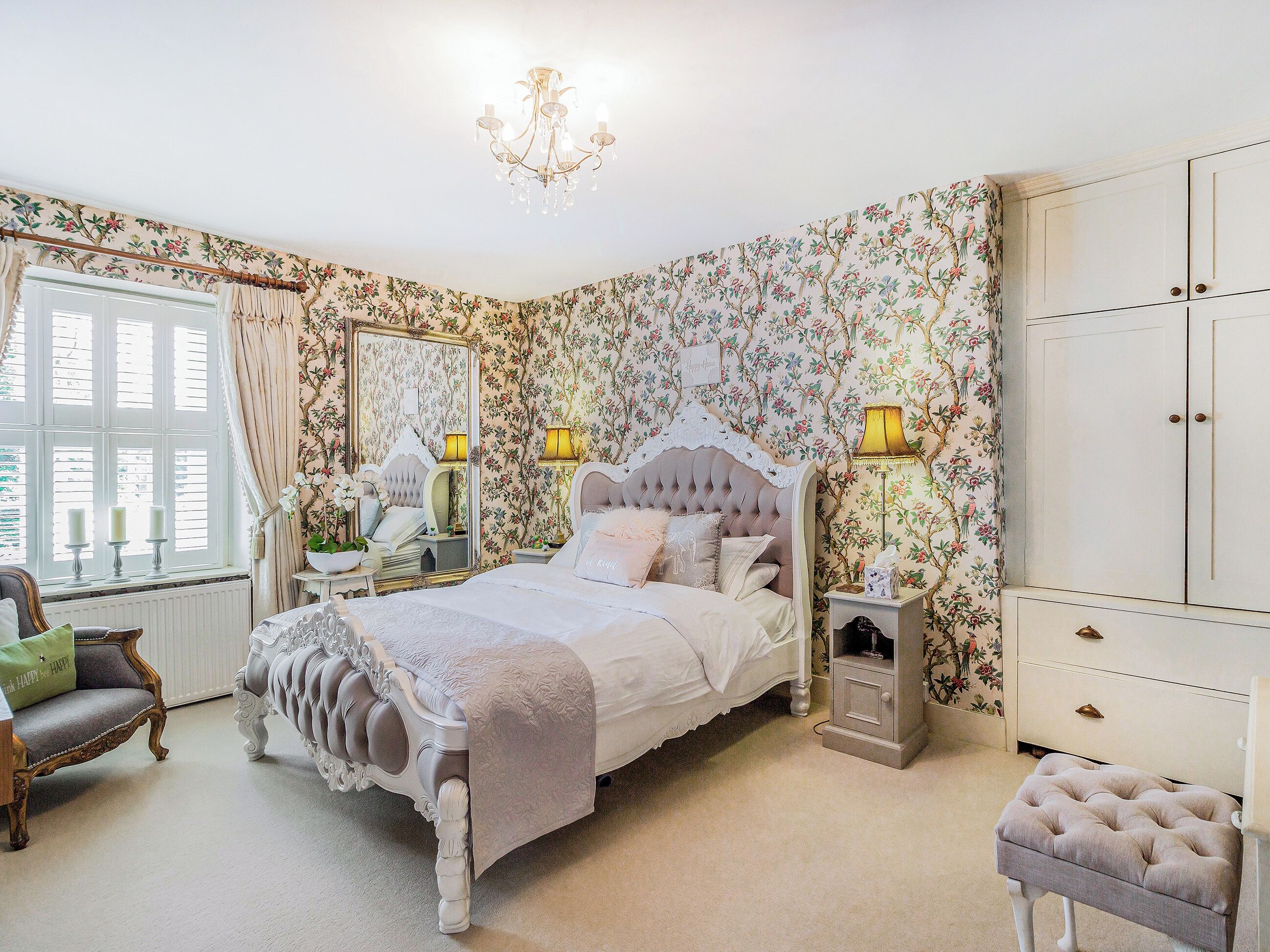 A bedroom with a four-poster bed, two bedside tables, a chair, a wardrobe, and a chandelier.