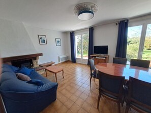A living room with a sofa, a coffee table, a TV, and a dining table with chairs.