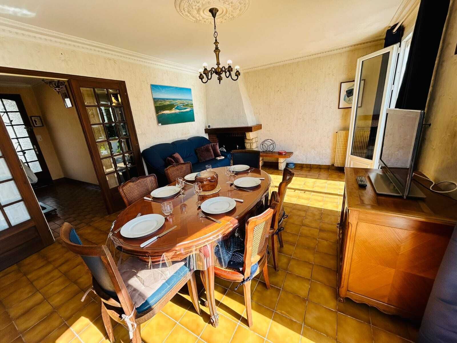 Ruokailutilassa on puinen pöytä, johon on katettu neljälle, koristeellinen kattokruunu ja ikkunasta avautuva näkymä joelle.