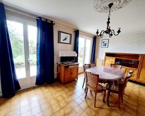 A dining area with a round table and chairs, a television on a wooden cabinet, and a chandelier.
