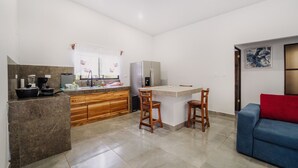 Een moderne keuken met een marmeren aanrecht, houten kastjes en een inbouwkoelkast. Er is een bar met krukken en een rode bank in de woonkamer.