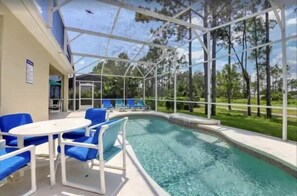 Un espace extérieur avec une piscine, des chaises bleues et une table, le tout entouré d’une structure en verre et d’arbres.