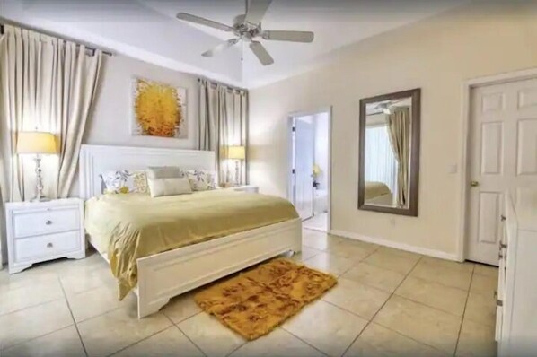 Une chambre à coucher avec un lit, des tables de chevet, un ventilateur de plafond, un miroir et une porte.