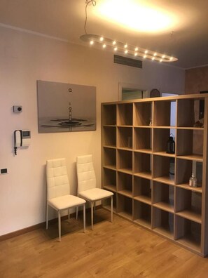 A room with two white chairs, a large wooden shelving unit, a ceiling light fixture, and a wall-mounted artwork.