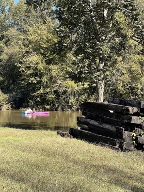 A calm river with kayaks, surrounded by dense trees and a grassy bank.
