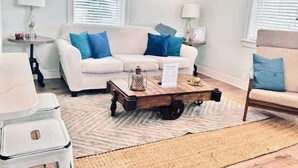 A living room with a white sofa, blue cushions, a coffee table, and a rug.