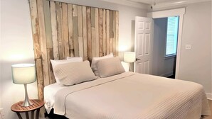 A bedroom with a wooden headboard, a bed with white bedding, two bedside lamps, and a door to the right.