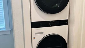 A stacked washer and dryer unit in a room with wooden flooring and a white door.