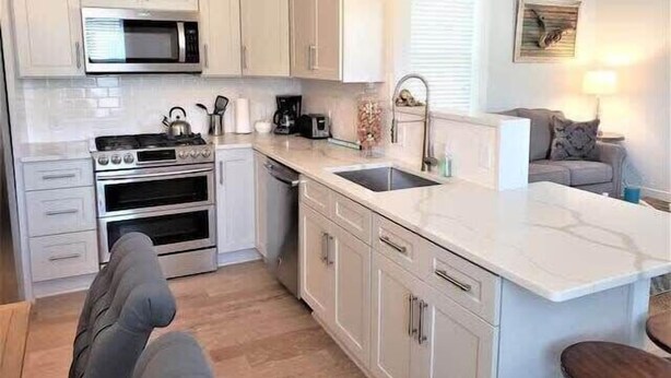A modern kitchen with white cabinetry, a built-in oven, a microwave, and a large island with a sink.
