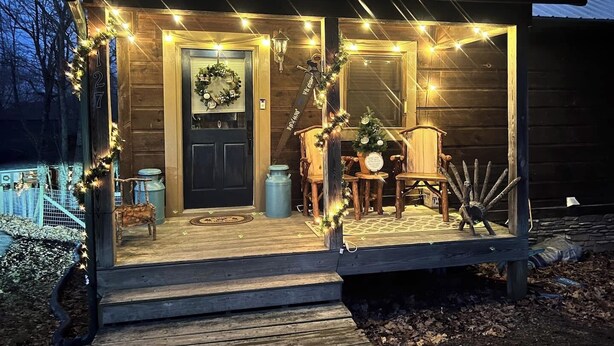 Eine Holz-Blockhütte mit Veranda, einer Tür mit Adventskranz und einem Weihnachtsbaum.