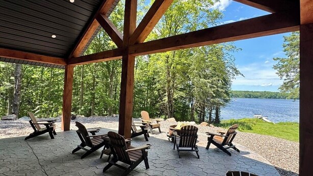 Ein überdachter Außenbereich mit Adirondack-Stühlen und Blick auf einen See.