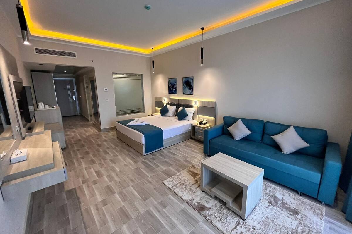 A modern hotel room with a bed, a blue sofa, a small coffee table, and a TV.