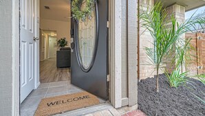 Una entrada moderna con una puerta oscura, felpudo y una pequeña planta en maceta.
