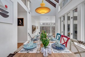 Un comedor con una mesa larga dispuesta para una comida, que incluye vasos de vidrio geométricos y sillas de colores.
