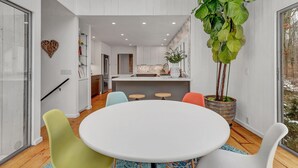 Een moderne eethoek met een ronde tafel, kleurrijke stoelen en een grote potplant.