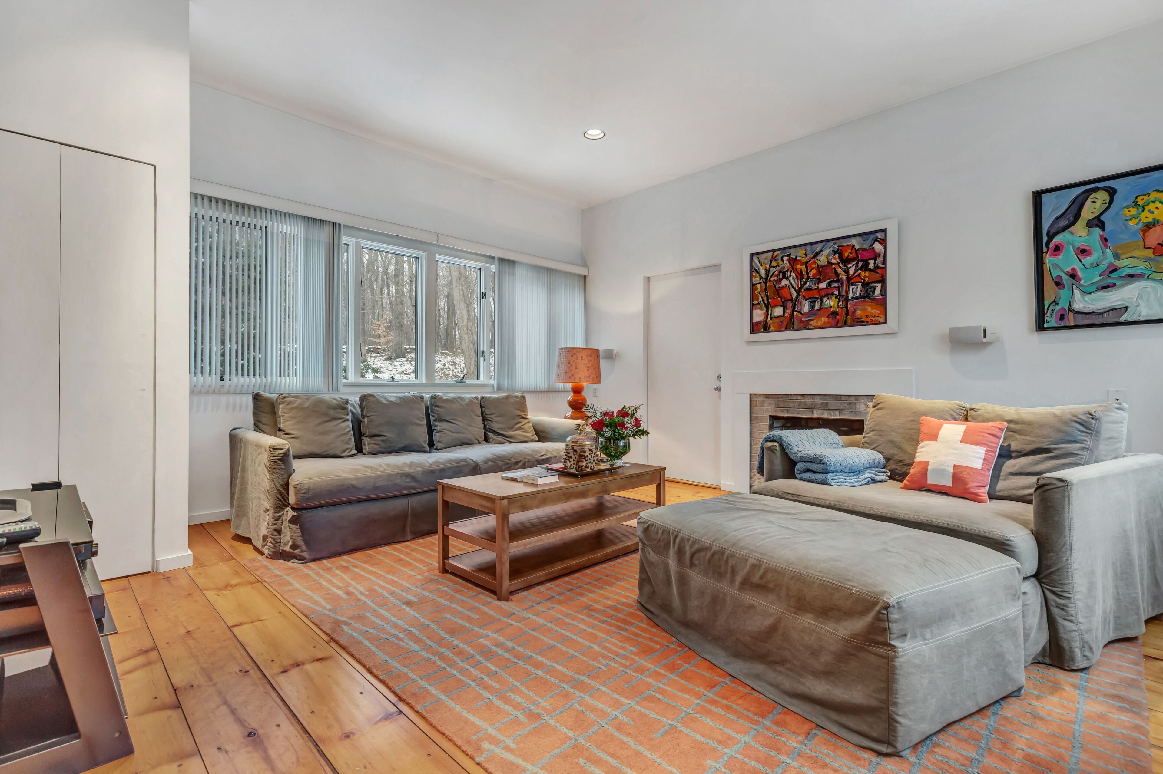 Un salon moderne avec un canapé, un pouf et une table basse, une cheminée et des œuvres d’art accrochées aux murs.