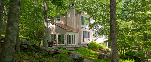 Una casa moderna con un amplio ventanal, rodeada por un bosque verde exuberante.