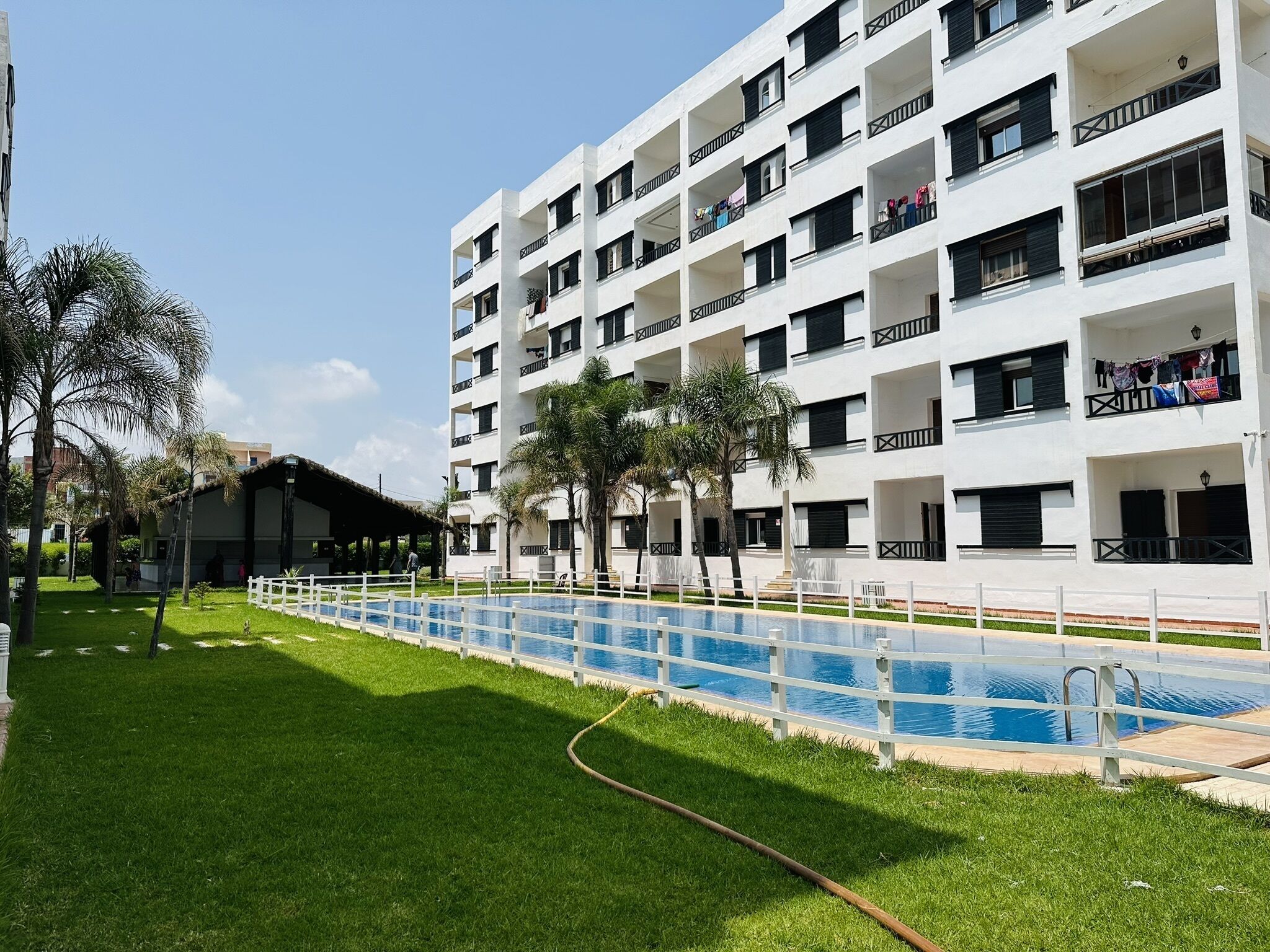 A multi-story building with balconies, a swimming pool, and a grassy area.