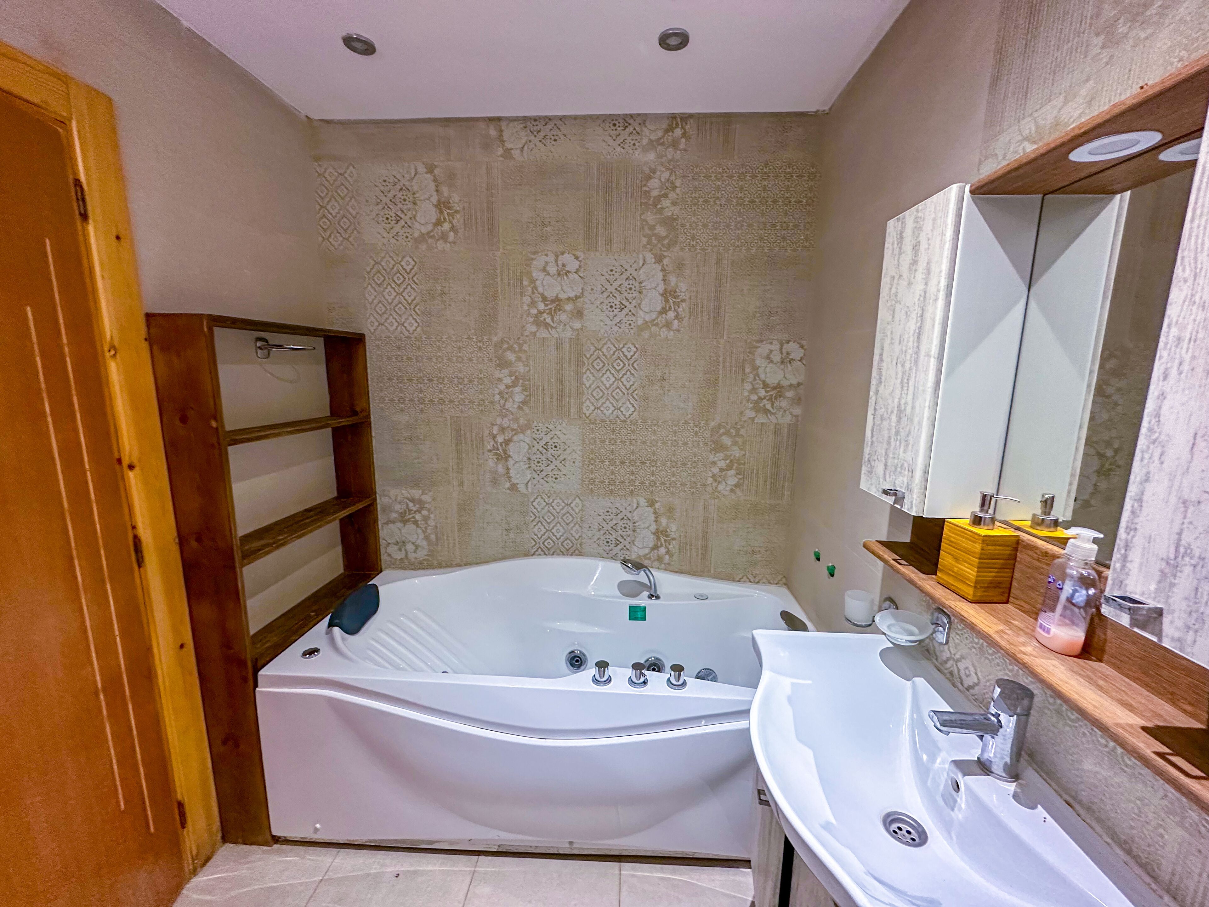 A bathroom with a bathtub, a sink, a mirror, and a wooden shelf with toiletries.