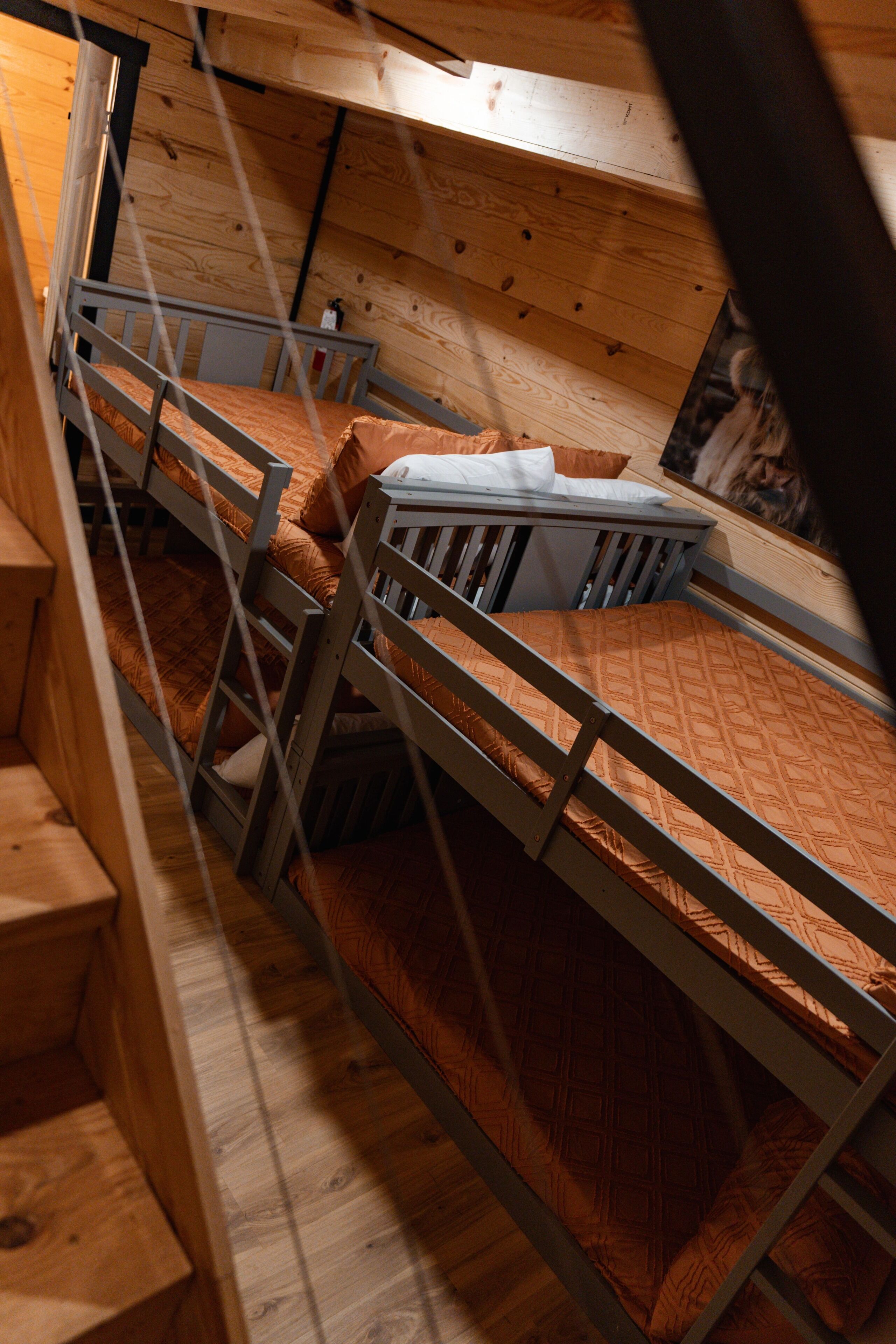 A bunk bed room with a wooden floor and walls, a small desk, and a poster on the wall.