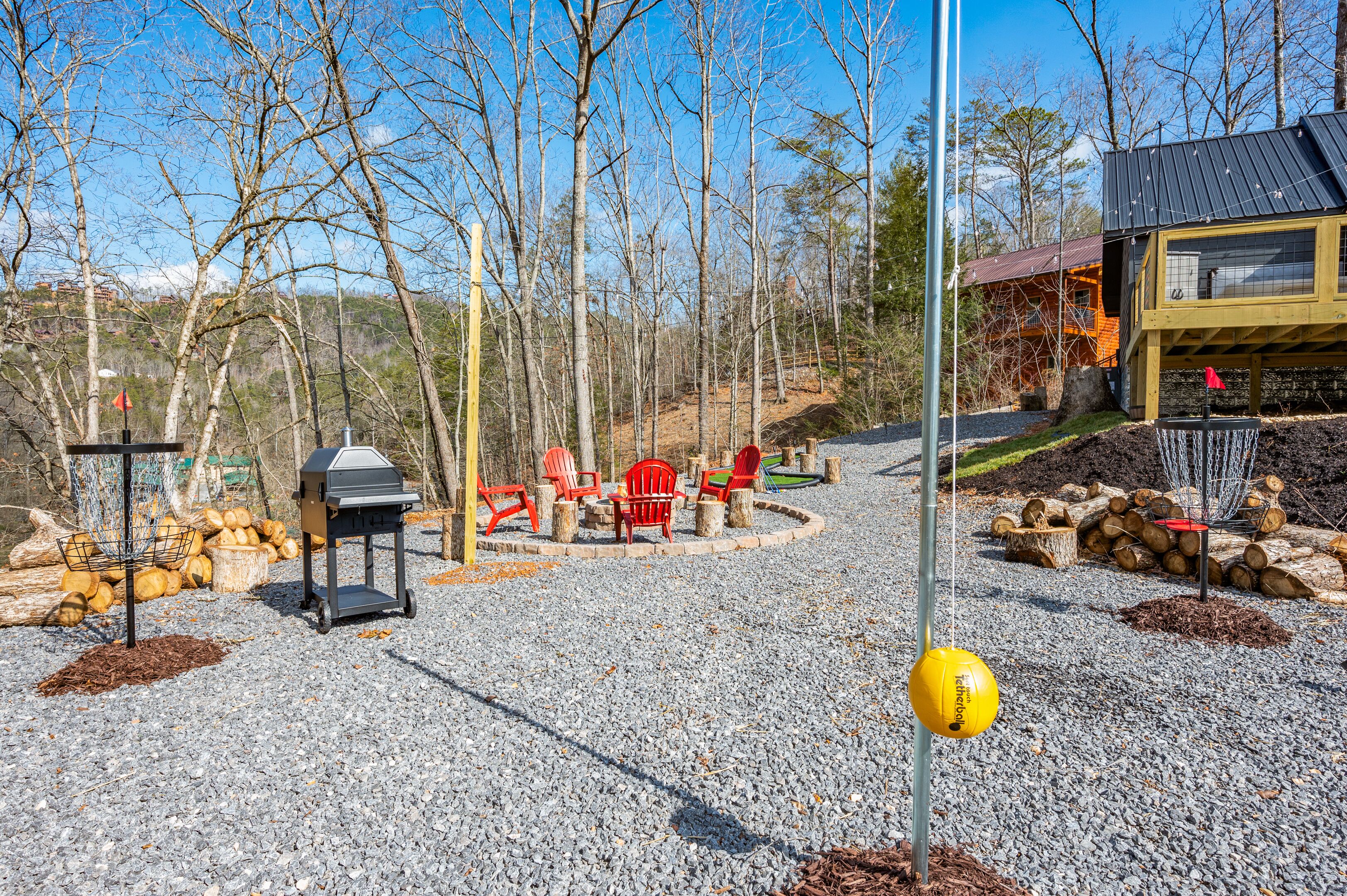 A gravel patio with red Adirondack chairs, a grill, and a yellow bollard.