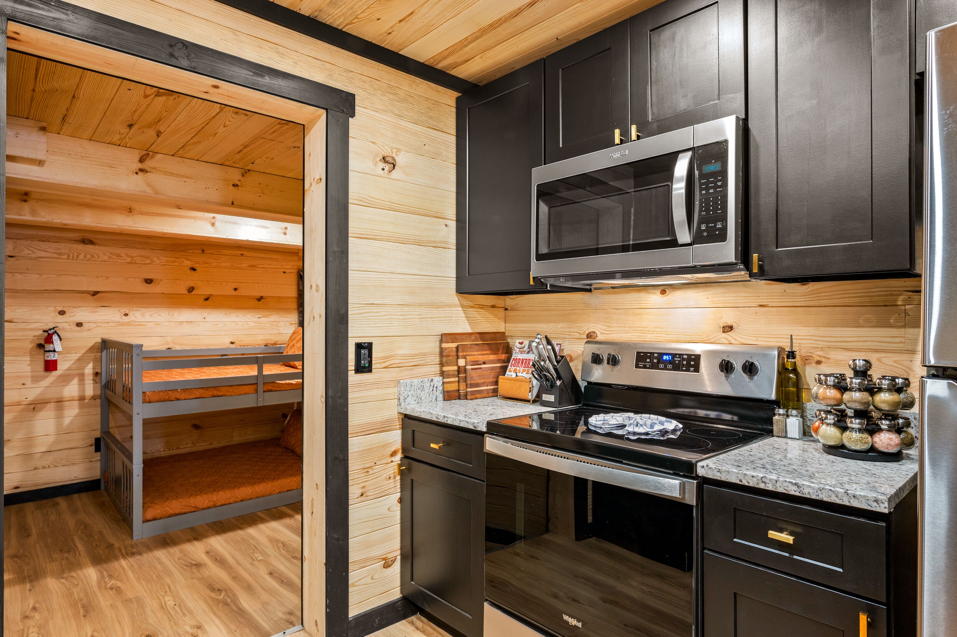 A compact kitchen with wooden walls, a microwave, stove, and a refrigerator.