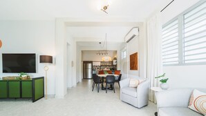 A modern living room with a flat-screen TV, a green cabinet, and a dining area with a table and chairs.