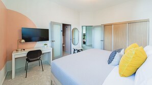 A bedroom with a bed, a desk, a chair, a TV, a mirror, and a wardrobe.