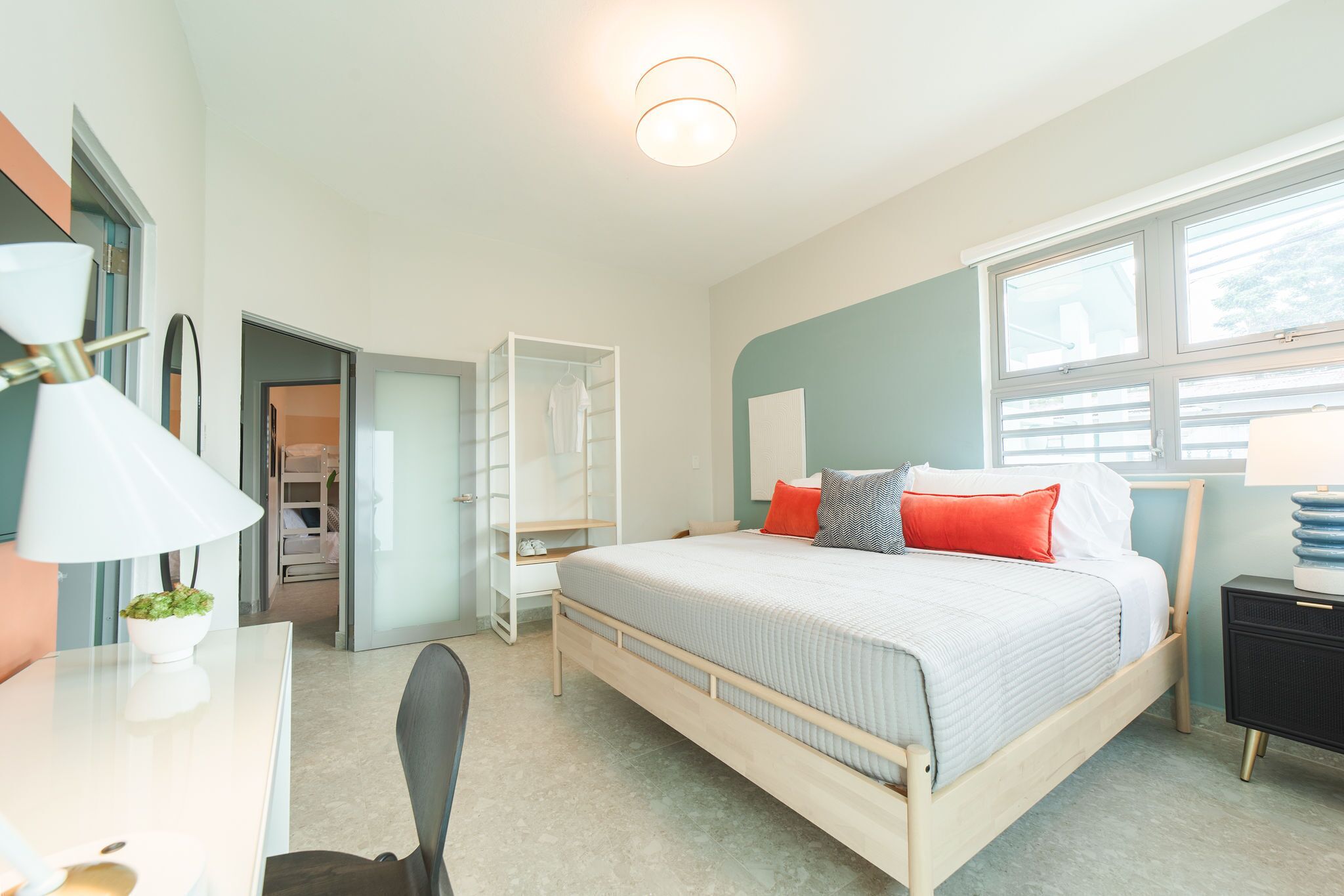 Ein modernes Schlafzimmer mit Bett, Nachttisch, Lampe und Blick ins Freie durch ein Fenster.