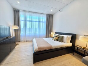 Una habitación de hotel con cama, televisión, escritorio y ventana con cortinas.