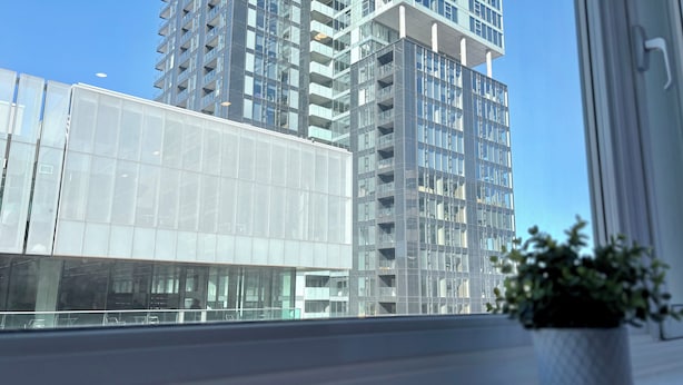 Een modern gebouw met grote glasramen en balkons, een heldere lucht en een potplant op de voorgrond.